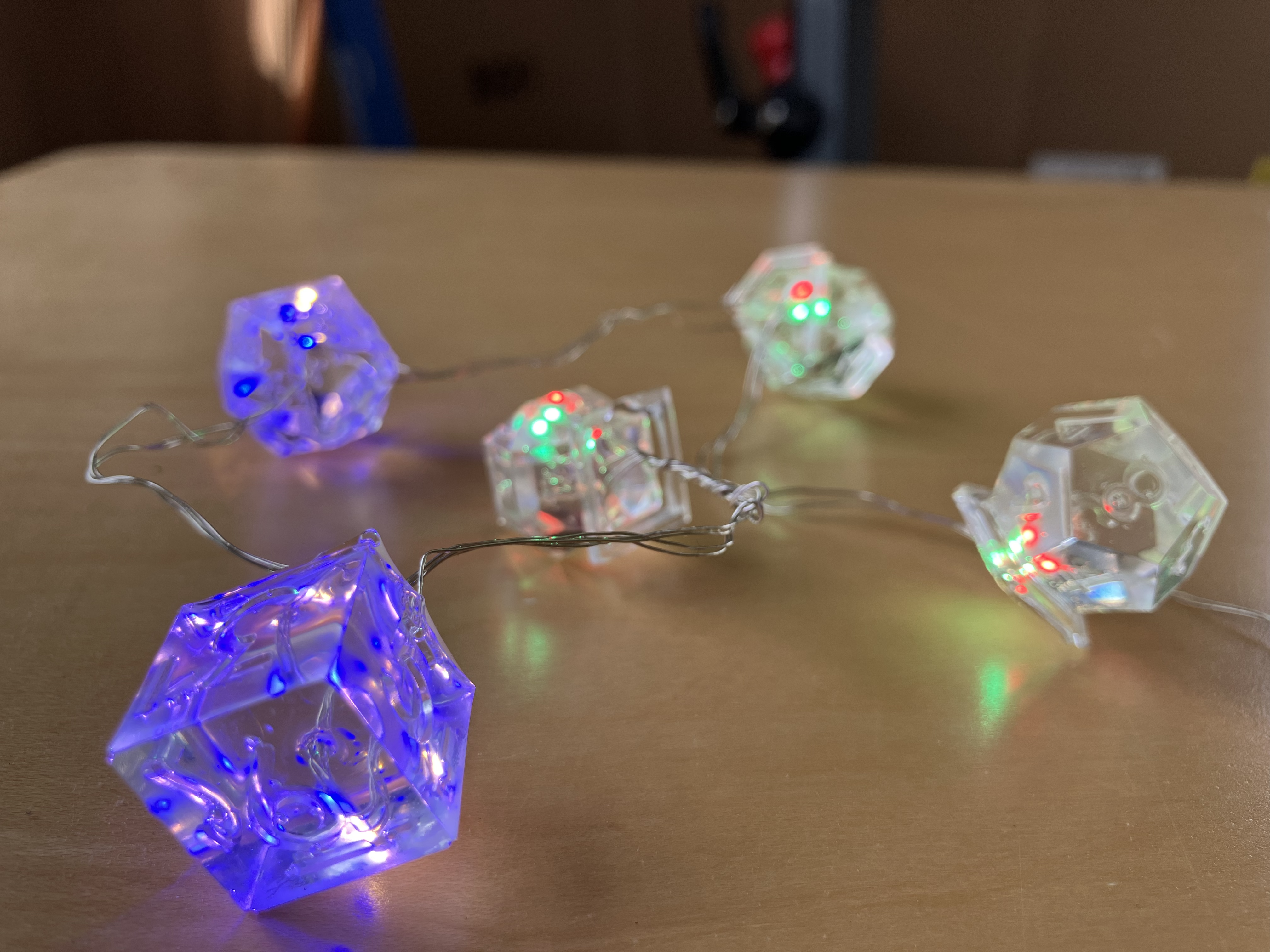 Photo of a necklace of TTRPG transparent resin dice lit up from inside with LEDs in various colors, laid out on a desk.