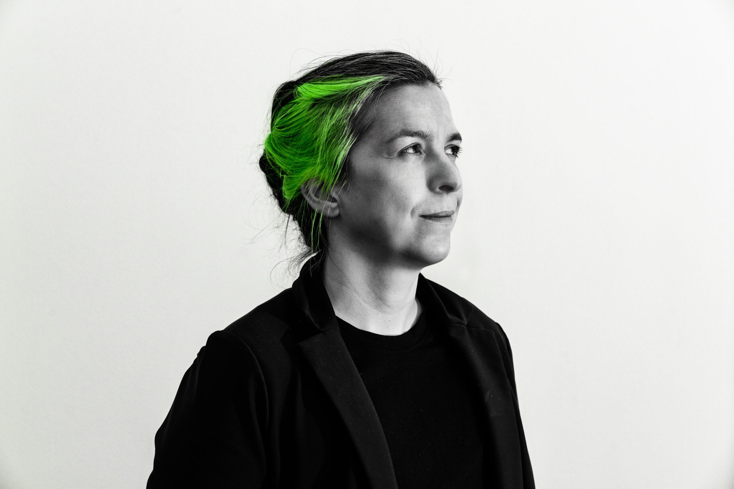 Headshot photo of Amanda Wyatt Visconti, edited to grayscale except for the green-dyed piece of their hair